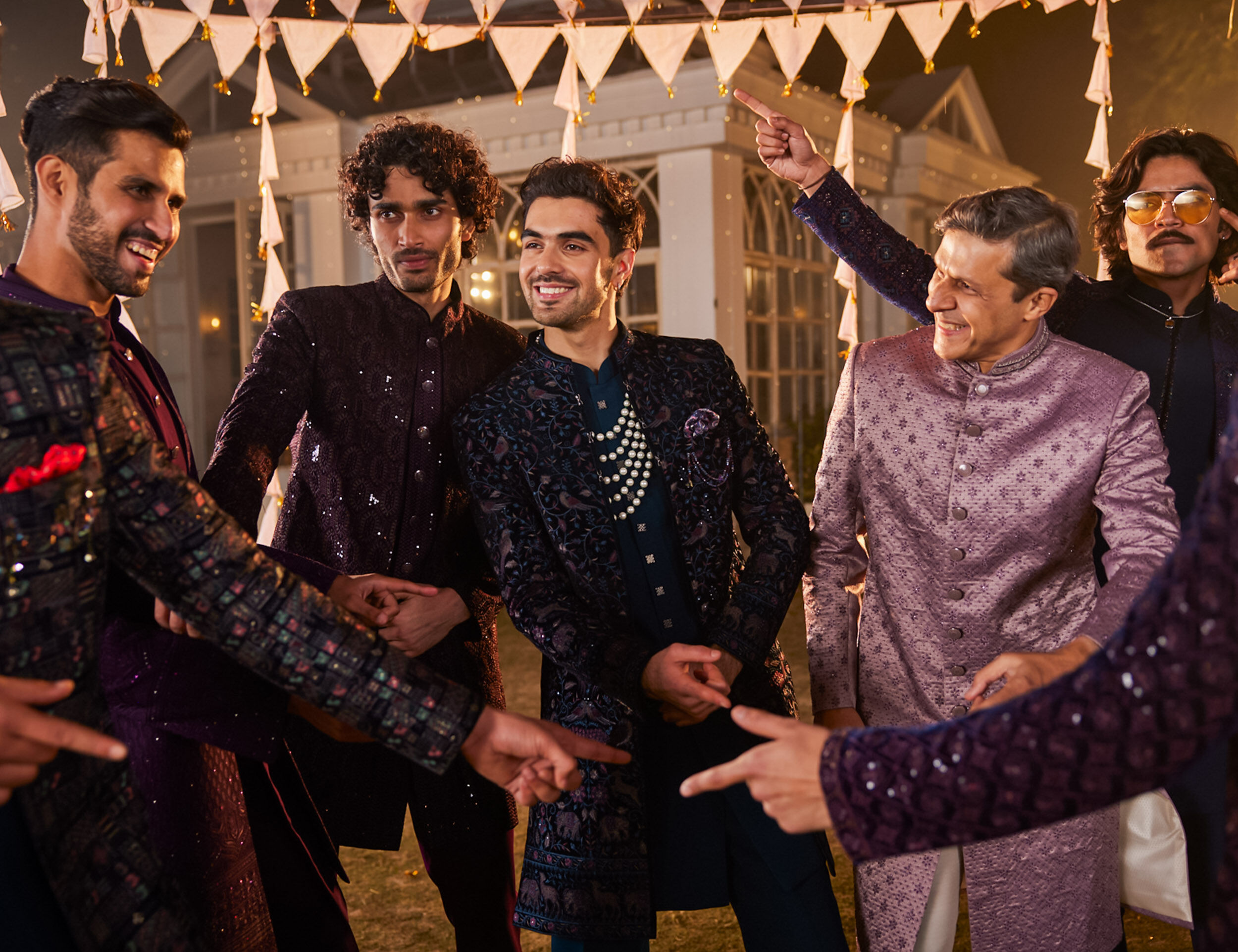 Group of men dressed in modern sherwanis and Indo-western outfits having fun and dancing during a lively sangeet night celebration